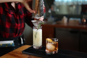 A bartender pouring a cocktail with a rosemary garnish.